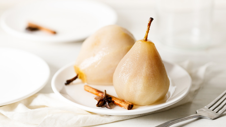 Poached pears on a white plate with a cinnamon stick and star anise on the side, on a white table