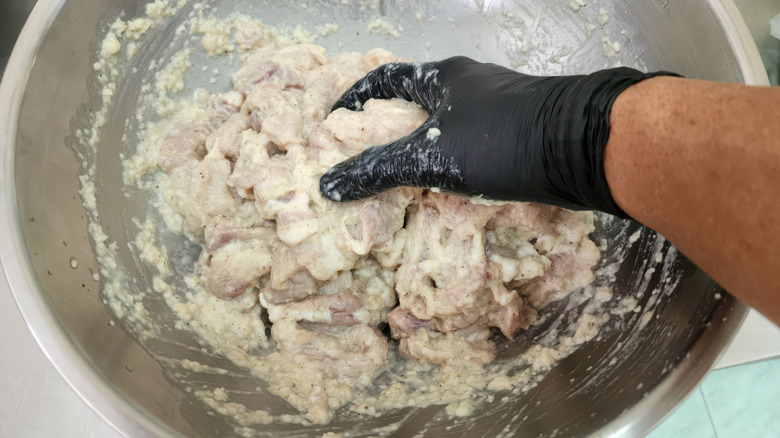 A person marinating meat in a stainless steel bowl