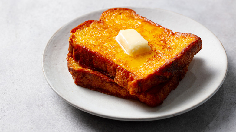 Two slices of French toast topped with butter on a white plate, placed on a table