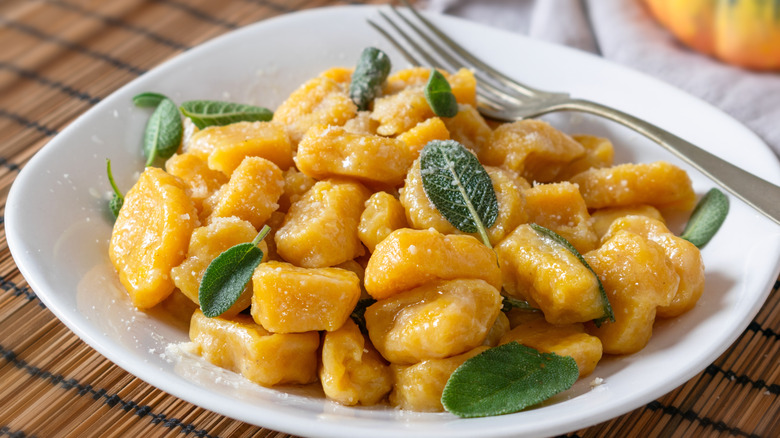 A plate of pumpkin gnocchi with fresh sage on a table with a fork on the side