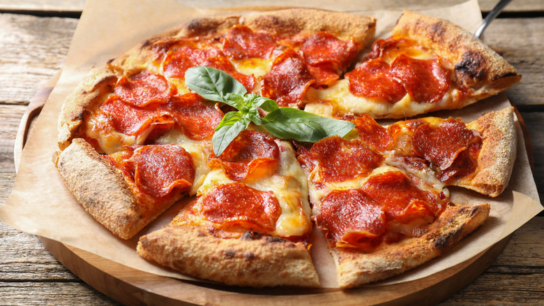 Pepperoni pizza on a piece of baking paper placed on a wooden board