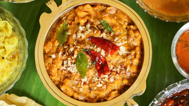 A bowl of pumpkin coconut curry topped with curry leaves and dried red chiles on a banana leaf