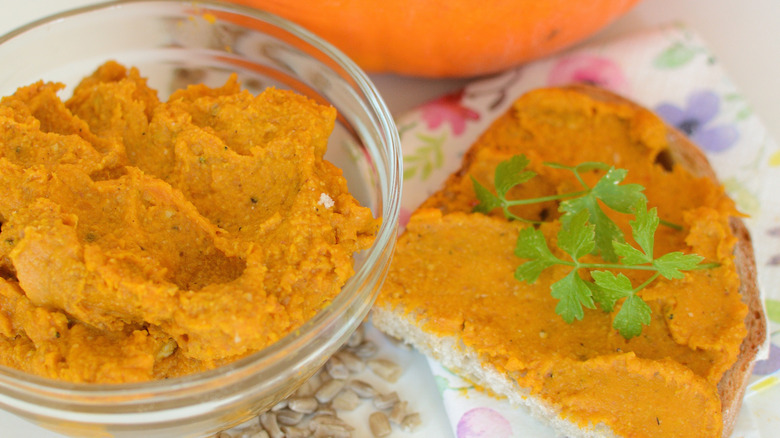 A bowl of pumpkin pesto with a slice of bread on the side