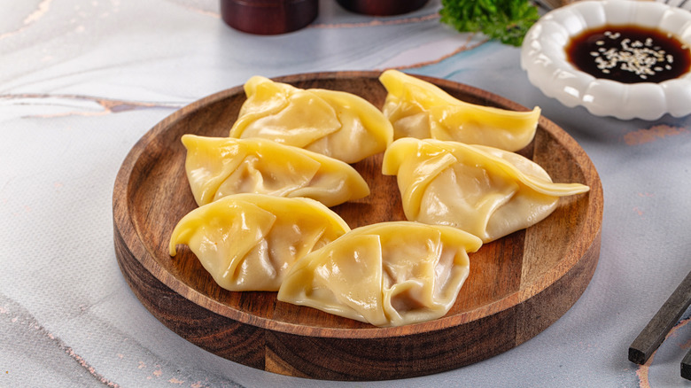 Steamed dumplings on a wooden platter placed on a marble table with a bowl of soy sauce on the side