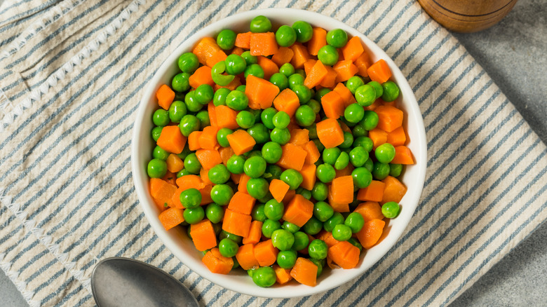 A bowl full of steamed carrots and peas on a table
