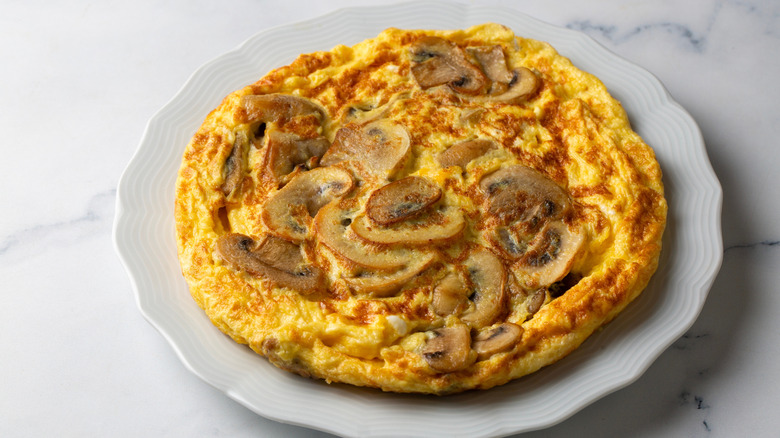A mushroom frittata on a white plate, placed on a marble table