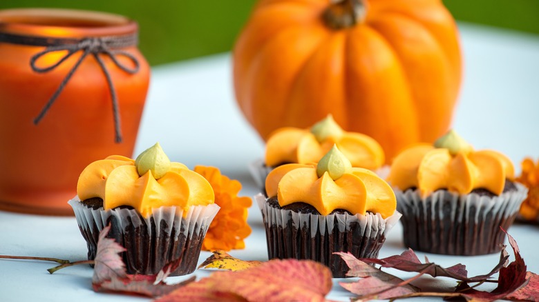 pumpkin cupcakes on a table with a pumpkin in the background