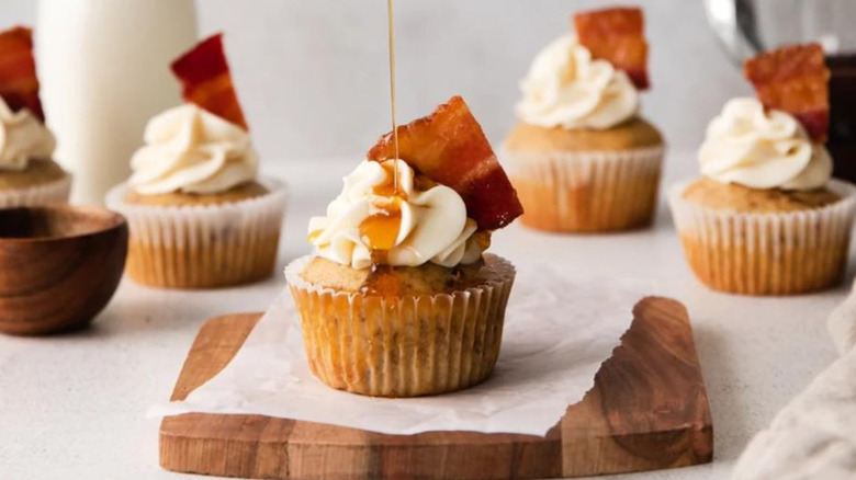 Cupcakes garnished with bacon and maple syrup on a cutting board and table