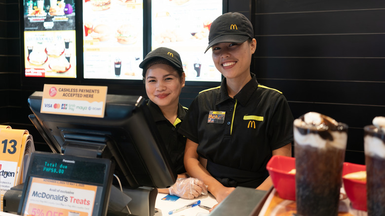 Two McDonald's crew members smile while standing behind the cash register