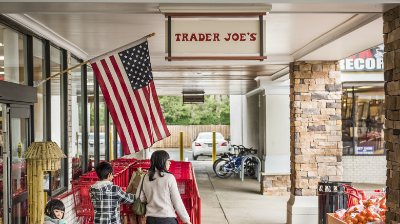 The outside of a storefront of Trader Joe's with an American Flag and a family of shoppers
