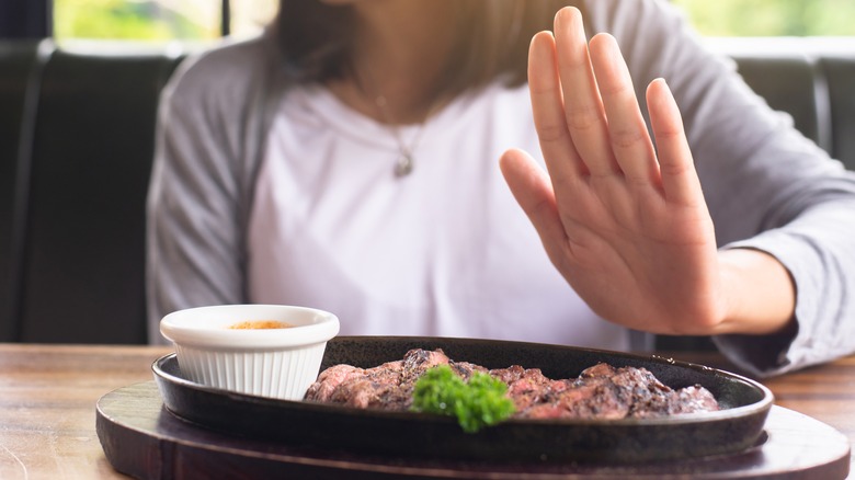 A woman politely passing on a plate of steak