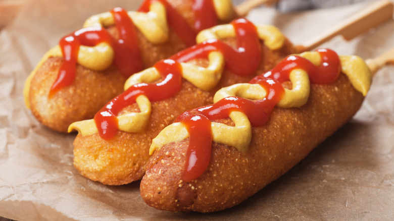 Close up of three corndogs drizzled with ketchup and mustard