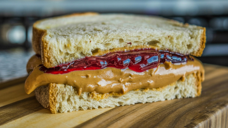 Close up of a halved peanut butter and jelly sandwiched on white bread sitting on a wooden board