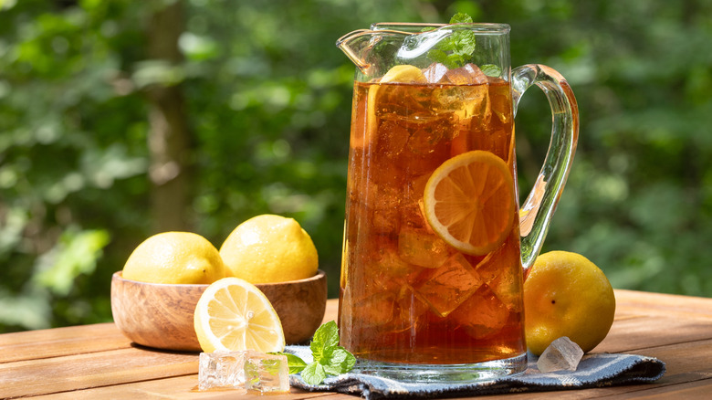 A pitcher of sweet iced tea next to some lemons on a wooden table outdoors