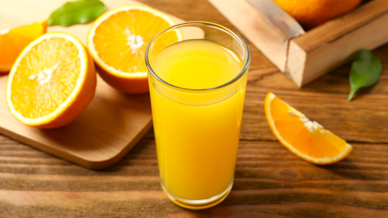 Orange juice in a glass placed on a wooden table with orange halves in the background