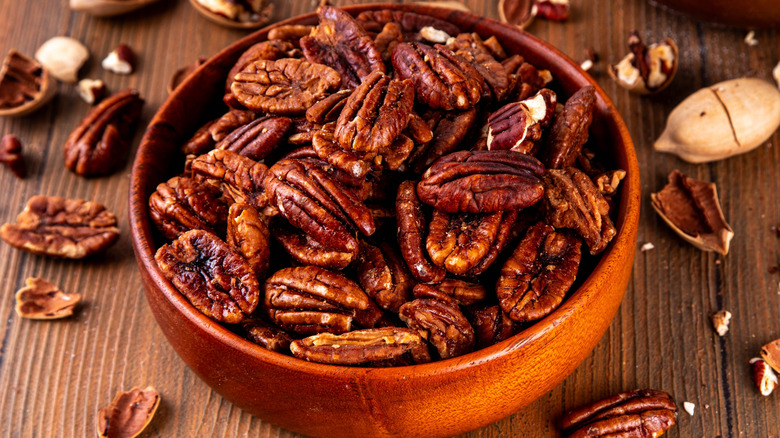 A bowl of caramelized pecan halves on a wooden table