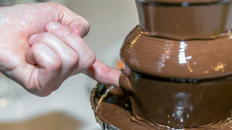 A man sticks his finger in a chocolate fountain