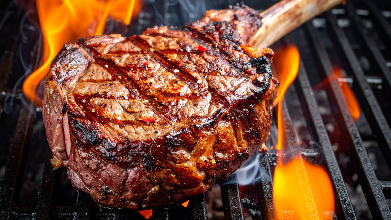 A close-up of a ribeye on a a flaming grill