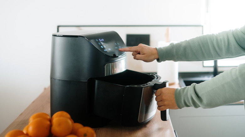 Person opening an air fryer basket with one hand, and pressing a button on the air fryer's console with the other