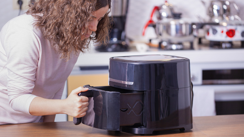 Woman holding open air fryer basket and peering inside
