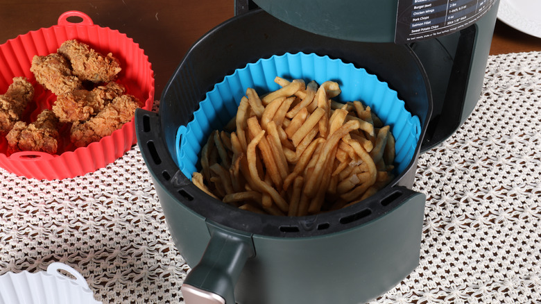 Air fryer with blue silicon liner with French fries inside, next to red silicon liner containing pieces of fried chicken