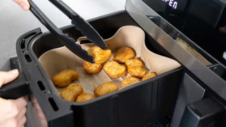 Person using tongs to lift chicken nugget out of air fryer