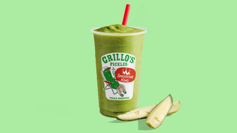 A green smoothie in a cup with the Grillo's Pickles logo on it, and two pickle spears to the side