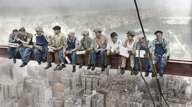 Color-restored vintage photograph of steelworkers eating lunch on a steel beam above New York City