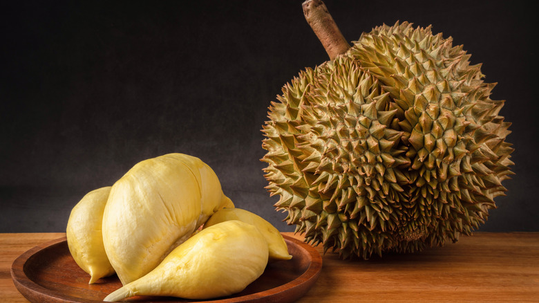 A whole durian on a wooden table with it's yellow flesh on the side