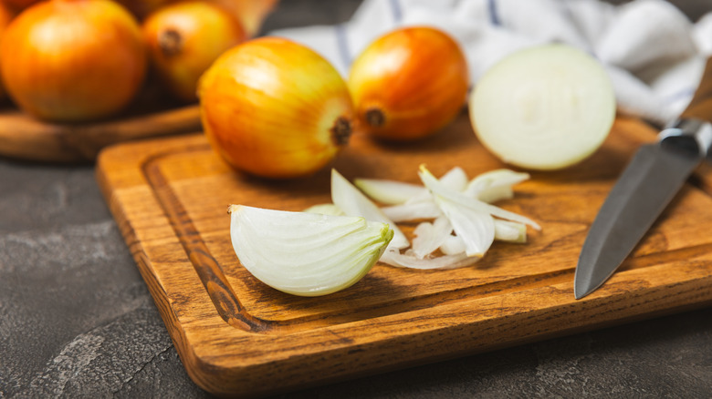 Sliced and whole onions on a wooden chopping board with a knife on the side