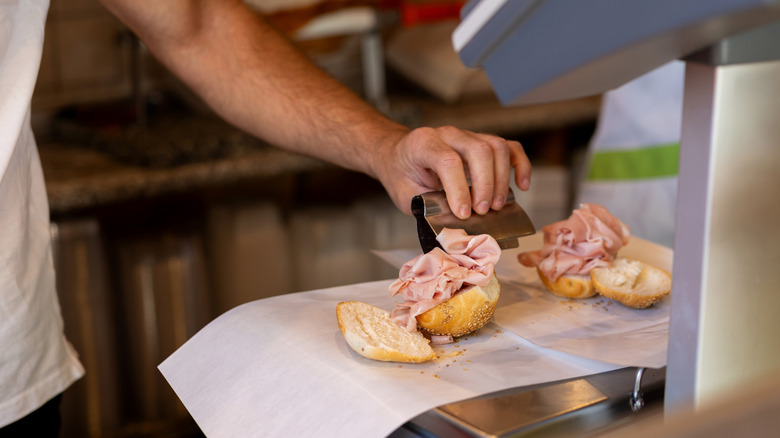 A chef puts together a deli sandwich on a slice of bread