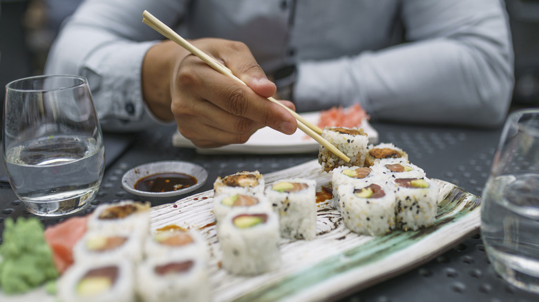 A person sits at a table eating sushi with chopsticks