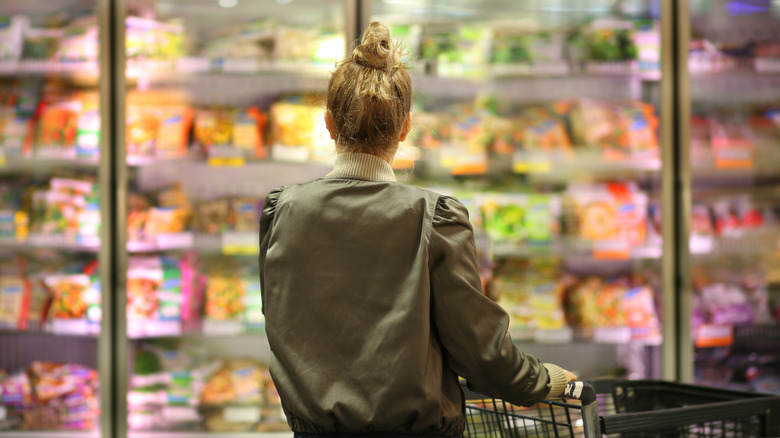 A woman is seen from behind, looking at frozen food in a supermarket