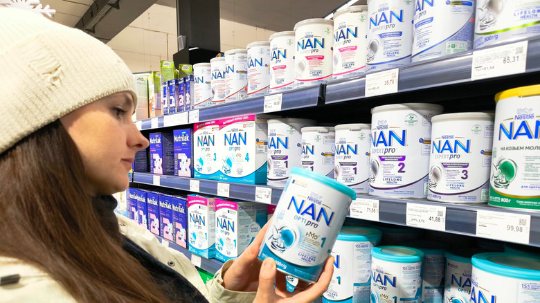 A woman examines a can of baby formula in a grocery store.
