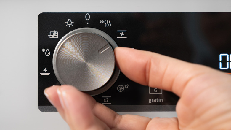 A person turning the knob on a modern kitchen oven