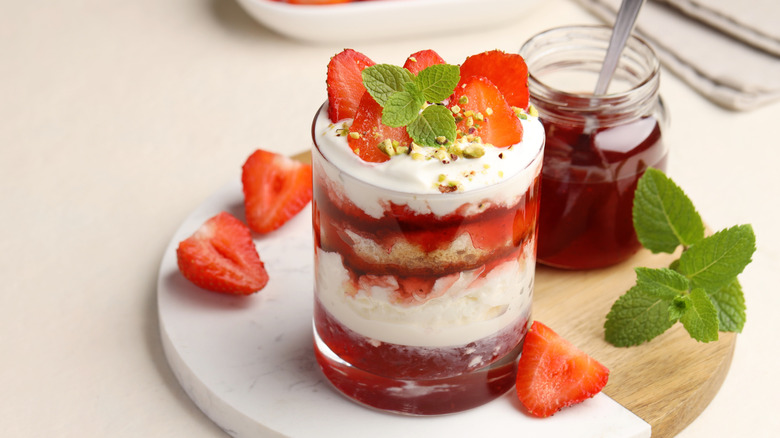 Strawberry trifle in a glass on a marble and wood serving board garnished with fresh strawberries and mint