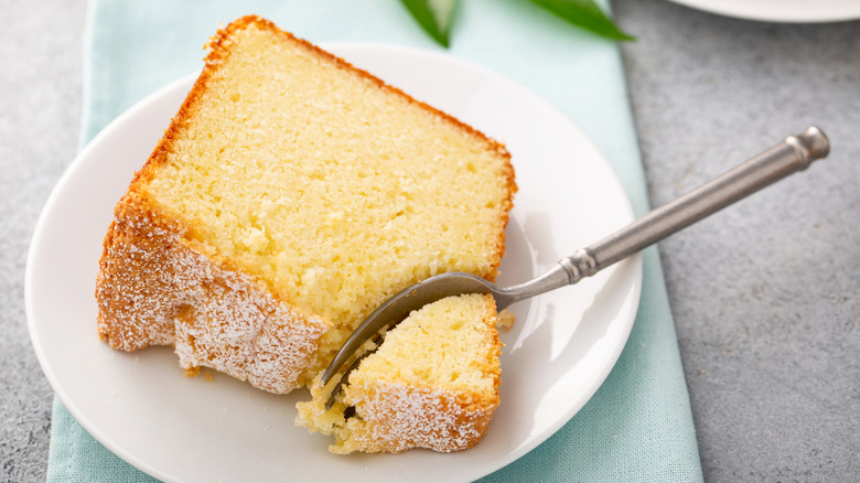 A slice of pound cake with a bite taken out of it on a white plate perched on a teal-colored napkin