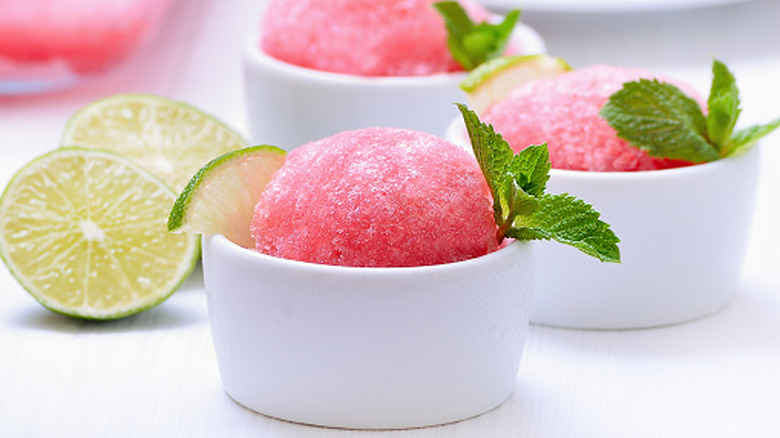 Small white bowls of watermelon granita garnished with lime slices and fresh mint
