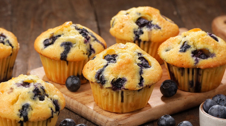Four blueberry muffins on a wooden cutting board