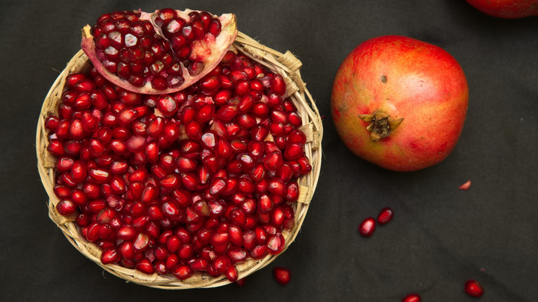 Pomegranate seeds in a basket, with half a pomegranate in a basket with a whole pomegranate on the side