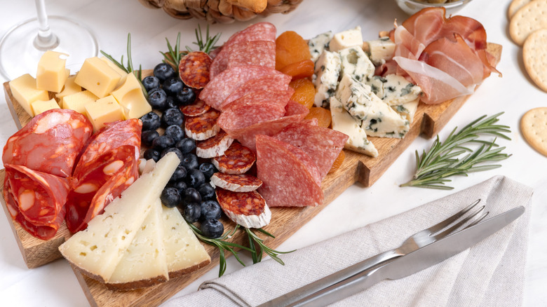 A charcuterie board with meat, cheese, blueberries, and dried apricots