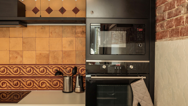 A brown terracotta tile backsplash in a modern, black kitchen