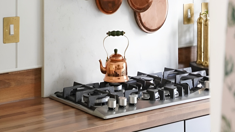 Copper cookware hanging from a gold pot rack mounted above the stove