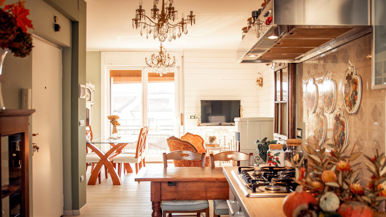 An Italian-style kitchen with a chandelier, tile backsplash, autumnal gourd arrangement, and window