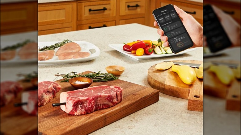 a smart thermometer in a steak with a hand holding a mobile phone showing the thermometer app