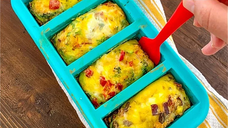 a hand placing food in a turquoise food storage tray