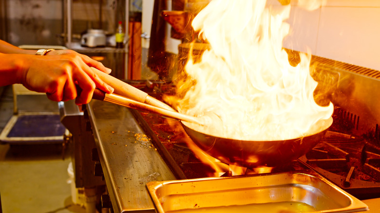 A chef handles a flaming wok in a kitchen.