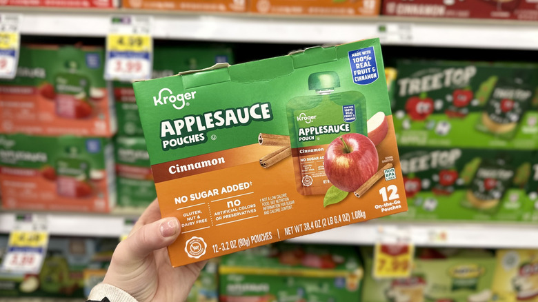 A hand holding a box of Kroger cinnamon-flavored applesauce pouches