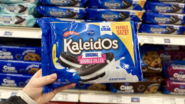 A hand holds a package of Kroger Kaleidos double-filled cookies in the cookie aisle