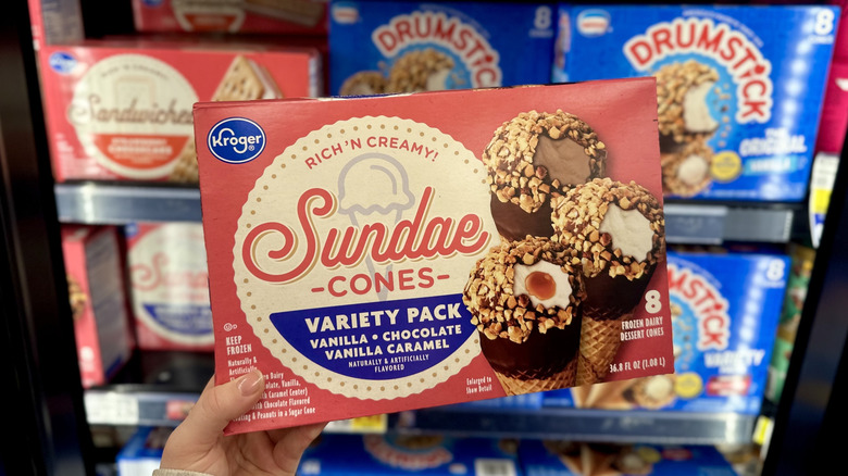 A hand holding Kroger Rich 'N Creamy Sundae cones in the freezer aisle